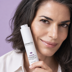 Frau hält die amerin REBORN straffende Gesichtscreme mit SymLift® in einer 50-ml-Airless-Flasche neben ihre Wange, vor lavendelfarbenem Hintergrund